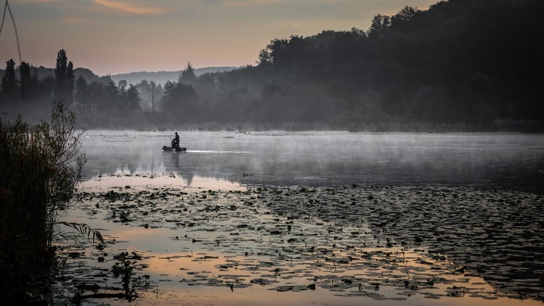 Person angelt im ruhigen See bei Morgennebel